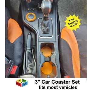 May include: Orange car coaster set, 3 inches in diameter, placed in a vehicle's cup holders. The coasters have a textured surface and are designed to fit most vehicles. The image also shows the car's interior.