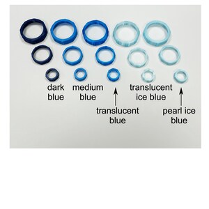 May include: A collection of blue rings in various sizes and shades, including dark blue, medium blue, translucent blue, translucent ice blue, and pearl ice blue. The text labels each color. The rings are arranged on a white surface.