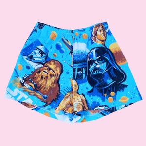 May include: Blue Star Wars themed shorts featuring a variety of characters including Darth Vader, Chewbacca, C-3PO, and Han Solo. The shorts have a white elastic waistband.