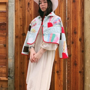 Peut inclure: Veste patchwork bleu clair avec bordure rouge et carrés de tissu colorés. La veste a une fermeture boutonnée sur le devant et est associée à un chapeau blanc et une robe crème. La veste est une pièce unique d'inspiration vintage.