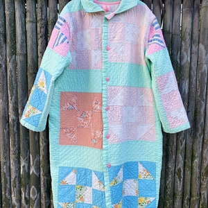 May include: A long, quilted robe with a button-up front. The robe is made of patchwork fabric in shades of pink, blue, and green. The fabric is quilted in a variety of patterns, including squares, triangles, and stars.