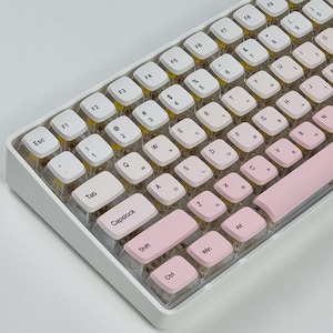 Könnte beinhalten: Eine weiße und rosa mechanische Tastatur mit einem Blumendesign auf den Tasten. Die Tastatur hat eine rosa Leertaste und eine rosa Escape-Taste.