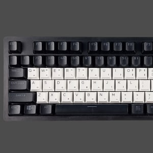 May include: A black and white mechanical keyboard with a white keycap set. The keyboard has a standard layout with function keys, number keys, and a numeric keypad. The keys have black lettering.