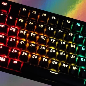 Könnte beinhalten: Eine schwarze Tastatur mit einem regenbogenfarbenen Hintergrundlicht. Die Tasten sind mit englischen und koreanischen Zeichen beschriftet. Die Tastatur verfügt über einen Ziffernblock und Funktionstasten.