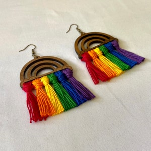 May include: A pair of rainbow-colored wooden earrings with rainbow-colored tassels. The earrings are shaped like rainbows and have a wooden base.
