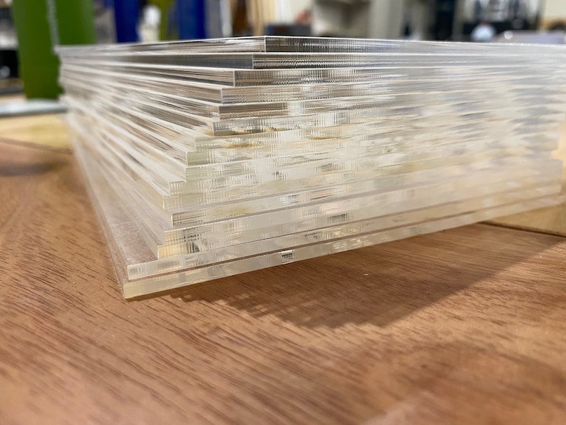 Puede incluir: Una pila de l&aacute;minas acr&iacute;licas rectangulares transparentes. Los bordes de las l&aacute;minas son visibles, creando un efecto de capas. Las l&aacute;minas est&aacute;n apiladas sobre una superficie de madera, con la luz reflej&aacute;ndose en los bordes.