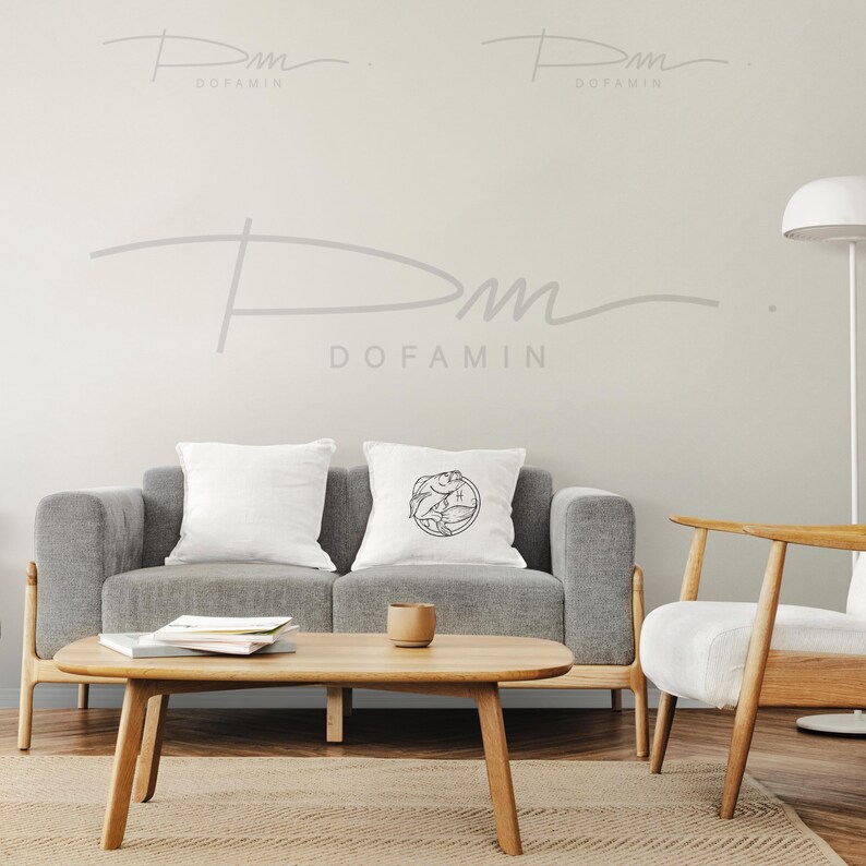 May include: A gray sofa with two white pillows, one with a black and white graphic design. A wooden coffee table with a book and a cup on it. A wooden chair with a white cushion. The wall behind the furniture is light gray with the text "Dofamin" written in gray.