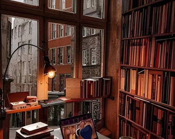 May include: A cozy home library with a large window overlooking a city street. A laptop sits on a desk with books, a lamp, and a teacup. Bookshelves are filled with books. The room has a warm, inviting atmosphere.