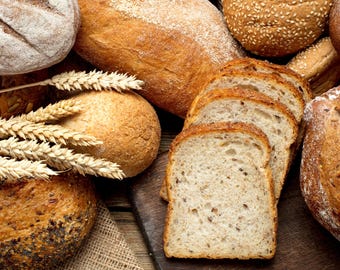 May include: An assortment of freshly baked bread, including loaves, rolls, and sliced bread. The bread has a golden-brown crust and a variety of textures, with some sprinkled with seeds. Wheat stalks are placed near the bread. The image conveys a rustic, bakery theme.