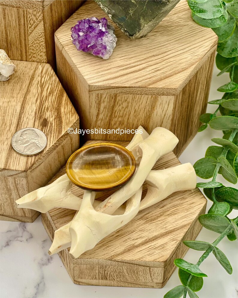 May include: A tiger's eye gemstone sits on a carved wooden stand, displayed on a wooden hexagonal block. A cluster of purple amethyst and a piece of pyrite are also visible. The image includes a US nickel coin and the text "Jayesbitsandpieces".