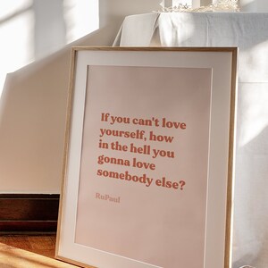 May include: A framed print with a pink background and a quote in bold red text: "If you can't love yourself, how in the hell you gonna love somebody else?"  The quote is attributed to RuPaul.