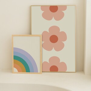 K&ouml;nnte beinhalten: Zwei gerahmte Kunstdrucke. Einer zeigt einen Regenbogen in Blau-, Gr&uuml;n-, Orange- und Gelbt&ouml;nen. Der andere hat drei gro&szlig;e rosa Blumen mit orangefarbenen Zentren auf cremefarbenem Hintergrund. Beide sind in hellen Holzrahmen.