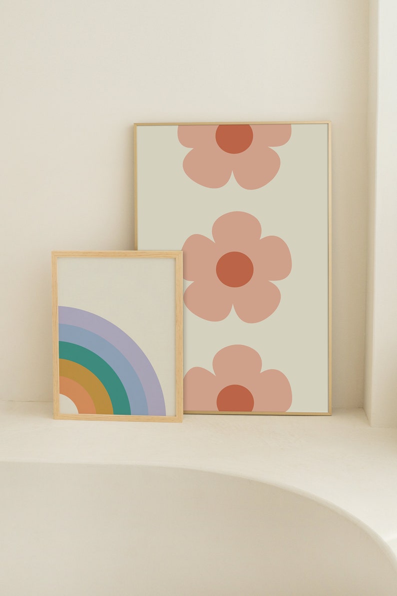 K&ouml;nnte beinhalten: Zwei gerahmte Kunstdrucke. Einer zeigt einen Regenbogen in Blau-, Gr&uuml;n-, Orange- und Gelbt&ouml;nen. Der andere hat drei gro&szlig;e rosa Blumen mit orangefarbenen Zentren auf cremefarbenem Hintergrund. Beide sind in hellen Holzrahmen.