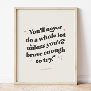 May include: A framed print with the quote "You'll never do a whole lot unless you're brave enough to try." in a bold, retro font. The print has a cream background with decorative star accents and the name "Dolly Parton" at the bottom.