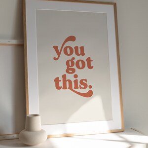 K&ouml;nnte beinhalten: Ein gerahmter Druck mit dem Text "you got this." in einer Retro-Orange-Schrift auf beigefarbenem Hintergrund.