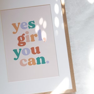 May include: A framed print with the text "yes girl, you can." in colorful, bold letters on a light pink background.