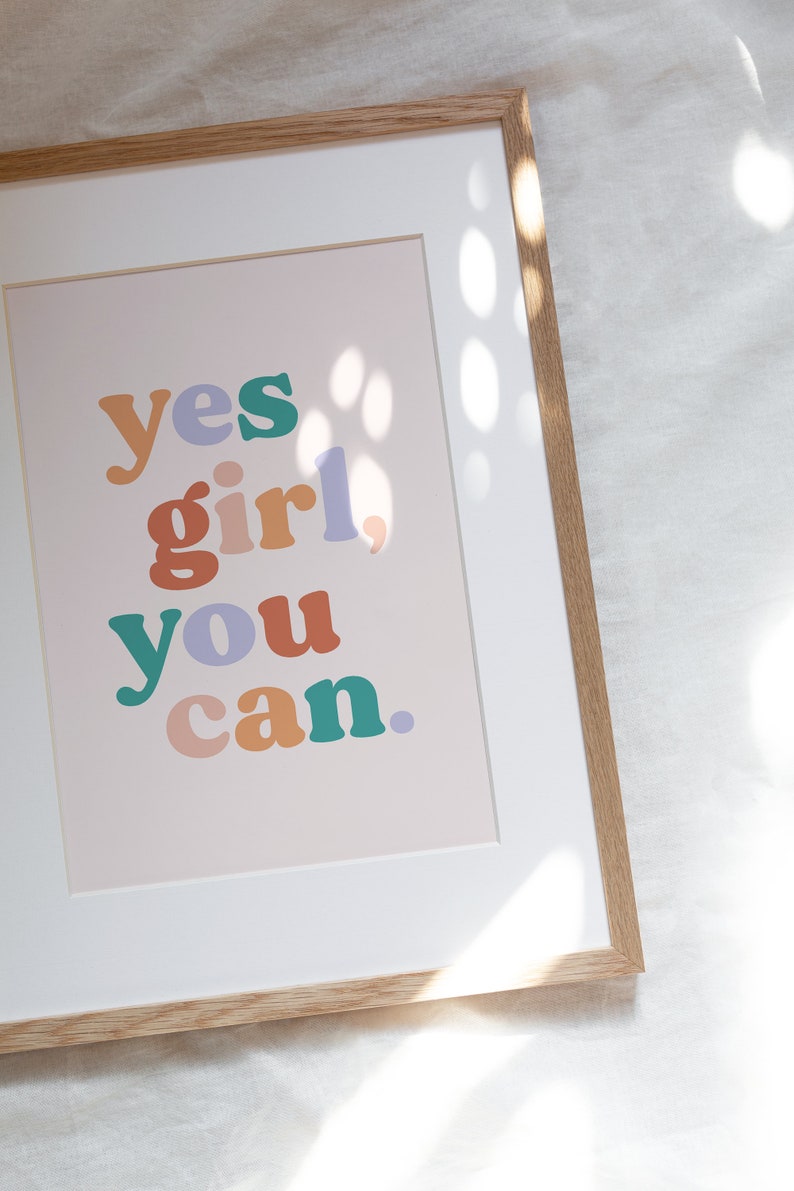May include: A framed print with the text "yes girl, you can." in colorful, bold letters on a light pink background.