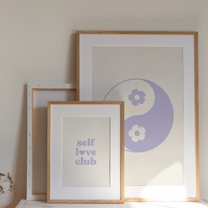 Może przedstawiać: Trzy oprawione wydruki na jasnobeżowym tle. G&oacute;rny wydruk przedstawia fioletowy symbol yin yang z białymi kwiatami. Środkowy wydruk zawiera tekst "self love club" fioletowymi literami z fioletowym sercem. Dolny wydruk jest pusty.