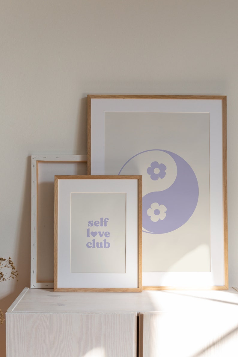 Może przedstawiać: Trzy oprawione wydruki na jasnobeżowym tle. G&oacute;rny wydruk przedstawia fioletowy symbol yin yang z białymi kwiatami. Środkowy wydruk zawiera tekst "self love club" fioletowymi literami z fioletowym sercem. Dolny wydruk jest pusty.