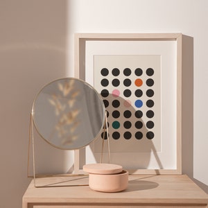 Puede incluir: Una mesa de tocador de madera clara con un espejo redondo dorado, una peque&ntilde;a caja de cer&aacute;mica rosa con tapa y una impresi&oacute;n enmarcada con un patr&oacute;n de lunares negros y blancos con lunares de colores.