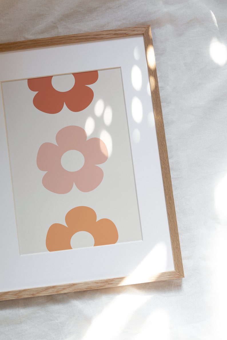 May include: A framed print with a white background and three stylized flowers in shades of orange, pink, and peach. The flowers have a simple, retro design.