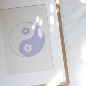 Może przedstawiać: Wydruk w ramie przedstawiający fioletowy symbol yin yang z białymi kwiatami wewnątrz każdej połowy symbolu. Wydruk jest na kremowym tle i jest oprawiony w jasną drewnianą ramę.