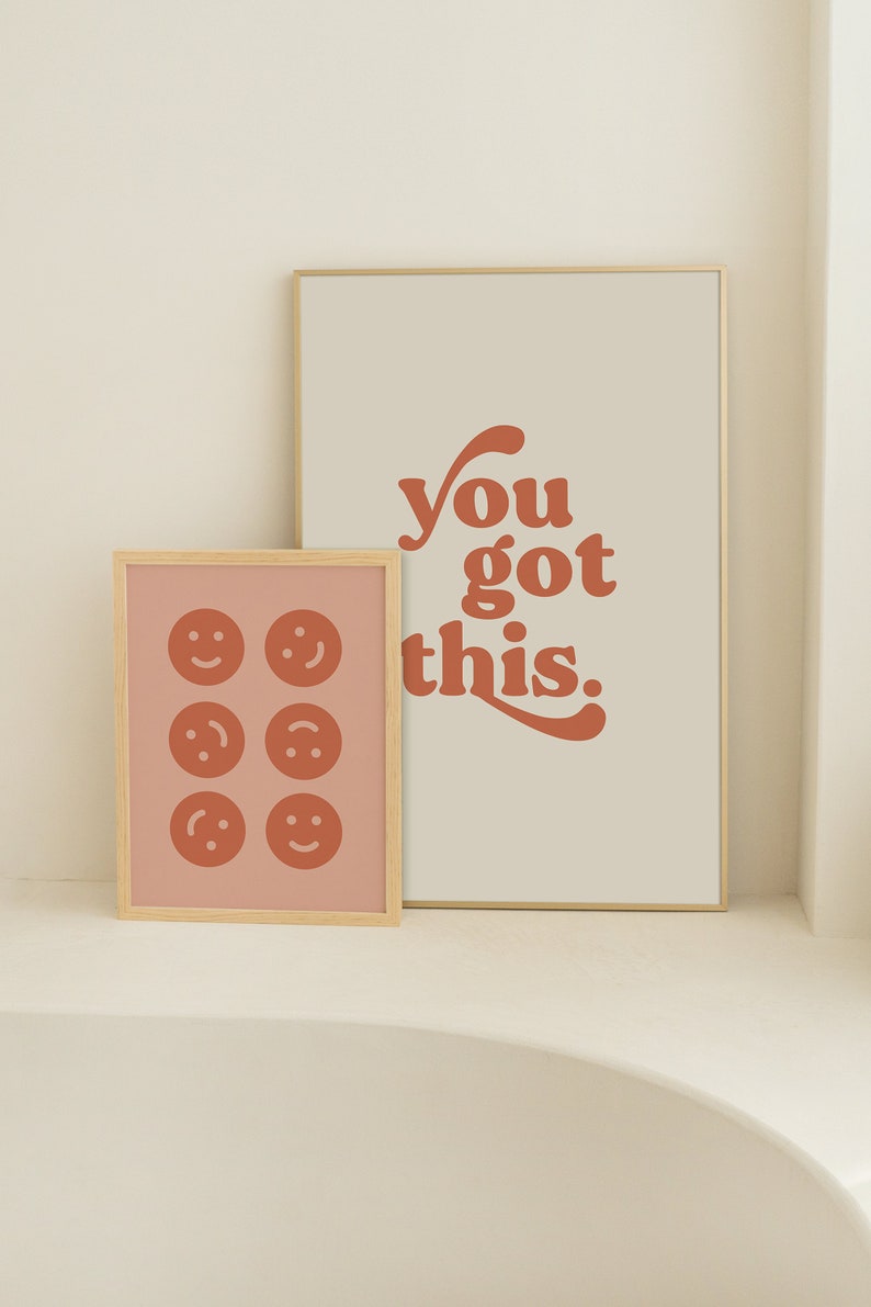 K&ouml;nnte beinhalten: Zwei gerahmte Drucke mit einer motivierenden Botschaft und einem Muster aus Smiley-Gesichtern. Der Druck links hat einen rosa Hintergrund mit sechs orangefarbenen Smiley-Gesichtern. Der Druck rechts hat einen beigefarbenen Hintergrund mit dem Text "you got this." in orange.