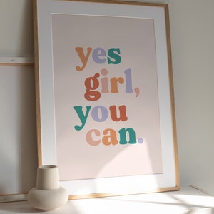 May include: A framed print with the text "yes girl, you can." in colorful, bold letters on a light pink background.