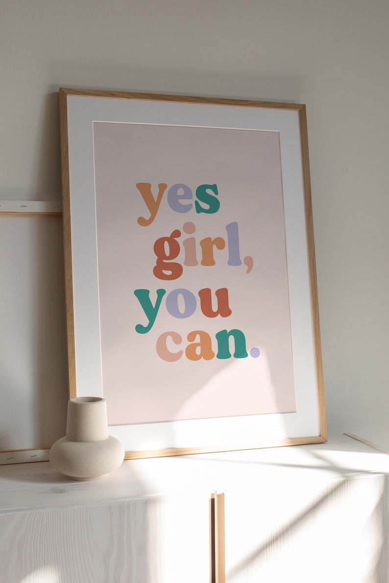 May include: A framed print with the text "yes girl, you can." in colorful, bold letters on a light pink background.