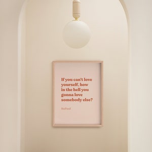 May include: A framed print with a pink background and a quote in brown text that reads "If you can't love yourself, how in the hell you gonna love somebody else?" The quote is attributed to RuPaul.
