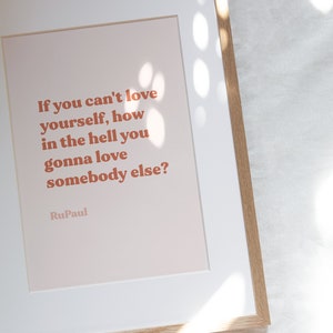 May include: A framed print with a peach background and a quote in orange text: "If you can't love yourself, how in the hell you gonna love somebody else?" - RuPaul