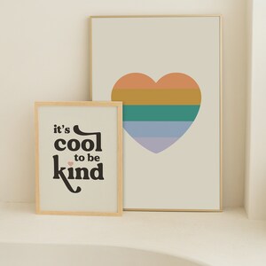 May include: Two framed prints with a minimalist design. The print on the left features the text "it's cool to be kind" in black with a small pink heart. The print on the right features a multi-colored heart with orange, yellow, green, and purple stripes.