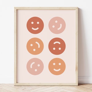 May include: A framed print featuring six different coloured smiley faces in shades of orange, red, and pink. The faces are arranged in a grid pattern.