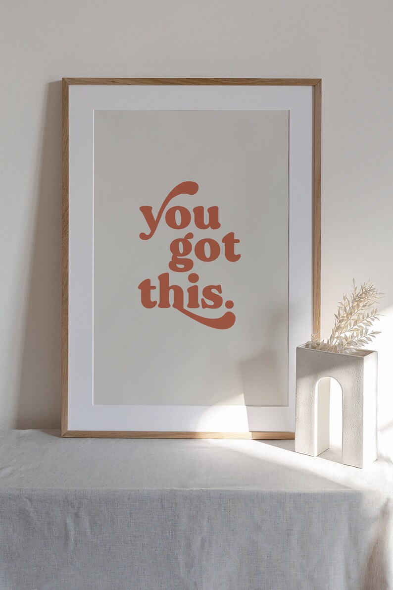 K&ouml;nnte beinhalten: Ein gerahmter Druck mit dem Text "you got this." in einem Retro-Schriftart-Stil. Der Text ist in einem verbrannten Orangeton auf einem hellbeigen Hintergrund. Der Rahmen ist in einer hellen Holzfarbe.