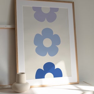 K&ouml;nnte beinhalten: Ein gerahmter Druck mit drei stilisierten Blumen in Blaut&ouml;nen und Lila. Die Blumen sind vertikal angeordnet, wobei die gr&ouml;&szlig;te Blume unten und die kleinste oben ist. Der Hintergrund ist hellbeige.
