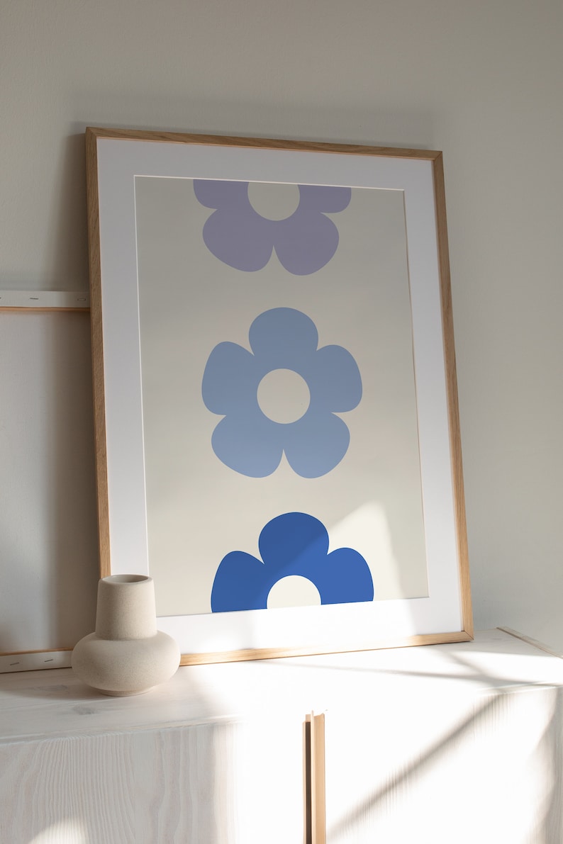 K&ouml;nnte beinhalten: Ein gerahmter Druck mit drei stilisierten Blumen in Blaut&ouml;nen und Lila. Die Blumen sind vertikal angeordnet, wobei die gr&ouml;&szlig;te Blume unten und die kleinste oben ist. Der Hintergrund ist hellbeige.