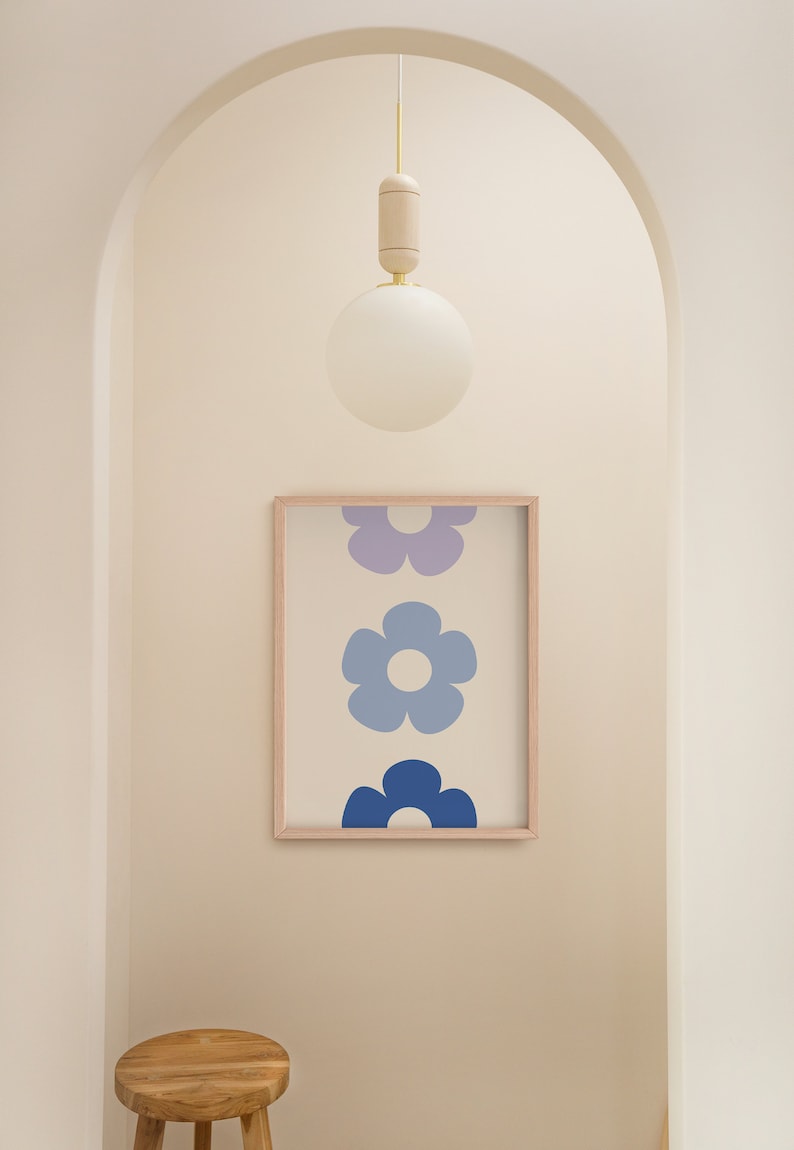 K&ouml;nnte beinhalten: Ein gerahmter Druck mit einer vertikalen Anordnung von drei stilisierten blauen und violetten Blumen. Der Druck h&auml;ngt an einer wei&szlig;en Wand in einem Flur mit einem Holzhocker im Vordergrund. Eine wei&szlig;e Kugel-Leuchte h&auml;ngt von der Decke.