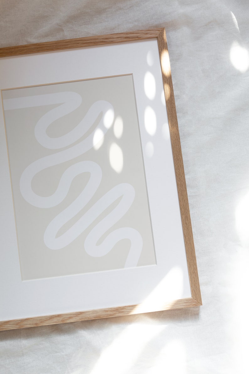 May include: A framed abstract print with a white line design on a light beige background. The frame is made of natural wood.