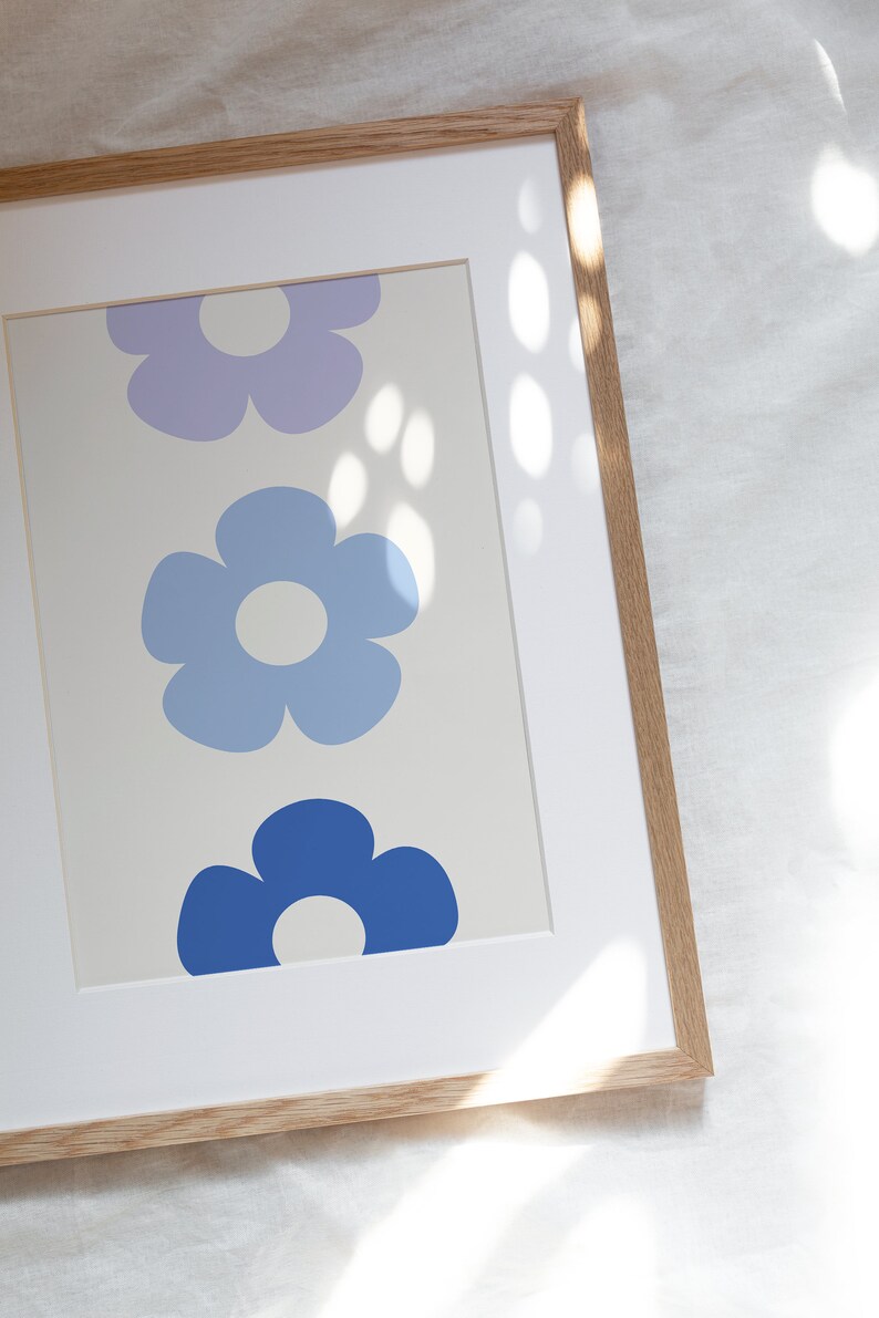 K&ouml;nnte beinhalten: Ein gerahmter Druck mit drei stilisierten Blumen in Blaut&ouml;nen und Lila. Die Blumen sind vertikal angeordnet, wobei die gr&ouml;&szlig;te Blume unten und die kleinste Blume oben ist.