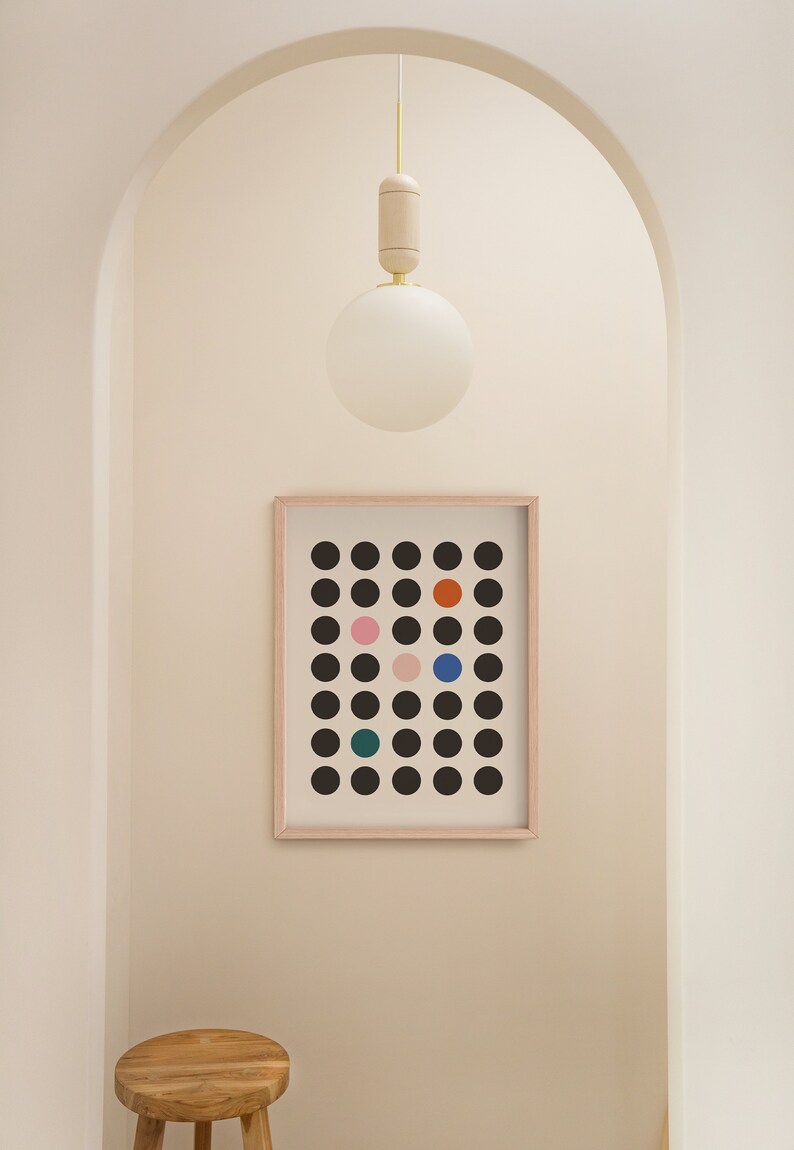 Puede incluir: Una impresi&oacute;n enmarcada de un dise&ntilde;o geom&eacute;trico en blanco y negro con c&iacute;rculos de colores. La impresi&oacute;n est&aacute; colgada en una pared blanca en un pasillo con un taburete de madera y una l&aacute;mpara de globo blanco.