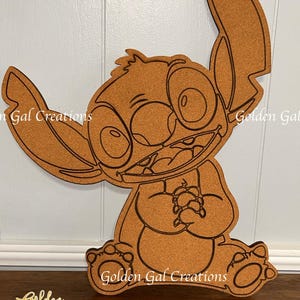 May include: A brown corkboard cutout of Stitch from Lilo & Stitch. The cutout is outlined in black and has a white background. The text "Golden Gal Creations" appears at the bottom of the image.
