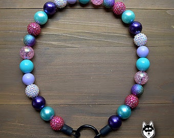 May include: A colorful beaded dog collar with a black metal clasp. The beads are in shades of pink, purple, turquoise, and white.