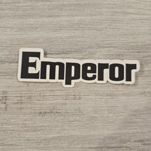 May include: Black and white sticker with the word "Emperor" printed in bold, uppercase letters.