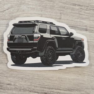 May include: A black SUV with a roof rack, seen from the back. The vehicle has black wheels with silver rims.