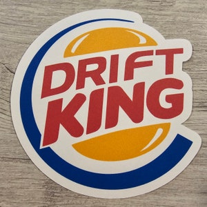 May include: A white sticker with a blue and yellow circle design. The text "DRIFT KING" is in red letters.