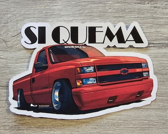 May include: A red pickup truck with the words "SI QUEMA" in black lettering on a white background. The truck has a black grille and a black bumper.