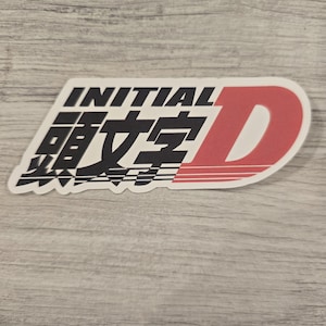 May include: A white sticker with black and red text. The text reads "INITIAL D" with Japanese characters below. The "D" is in red and the rest of the text is in black.