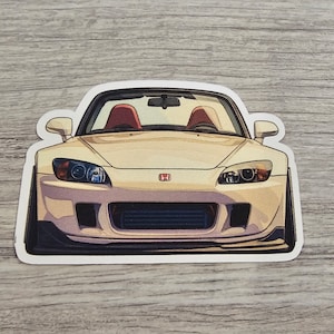 May include: A white Honda S2000 sports car with red interior. The car is facing the camera and the front grill is visible. The car is a popular model for car enthusiasts.