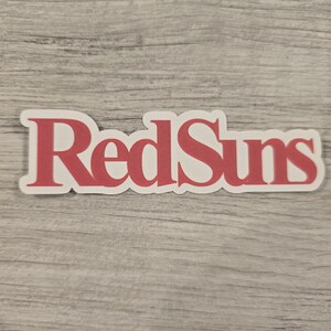 May include: RedSuns logo sticker in a red color on a white background.