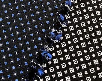 May include: Two fabric swatches with a black background and a repeating pattern of small white and blue squares. The swatches are sewn together at a diagonal angle.